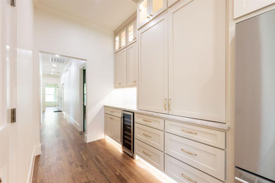 Custom cabinetry with gold-tone hardware, integrated wine refrigerator, integrated refrigerator, and light-toned countertop Custom cabinetry with gold-tone hardware, integrated wine refrigerator, integrated refrigerator, and light-toned countertop
