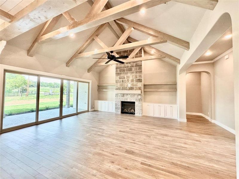 Unfurnished living room featuring high vaulted ceiling, beam ceiling, light wood finished floors, baseboards, and arched walkways