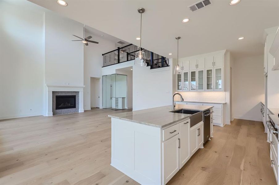 Kitchen featuring light wood-type flooring, light stone counters, white cabinets, a center island with sink, and ceiling fan