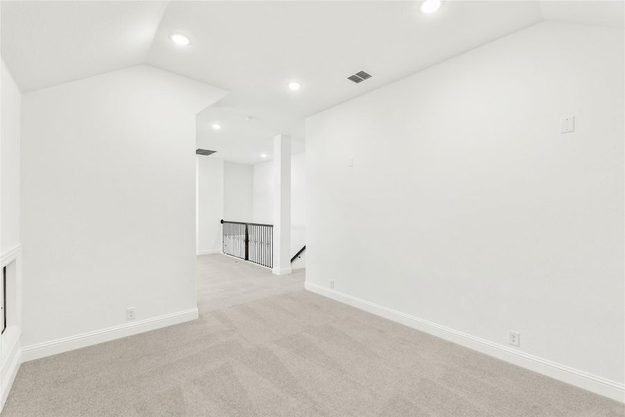 Empty upstairs loft with vaulted ceiling, carpet flooring, and black metal stair railing Empty upstairs loft with vaulted ceiling, carpet flooring, and black metal stair railing