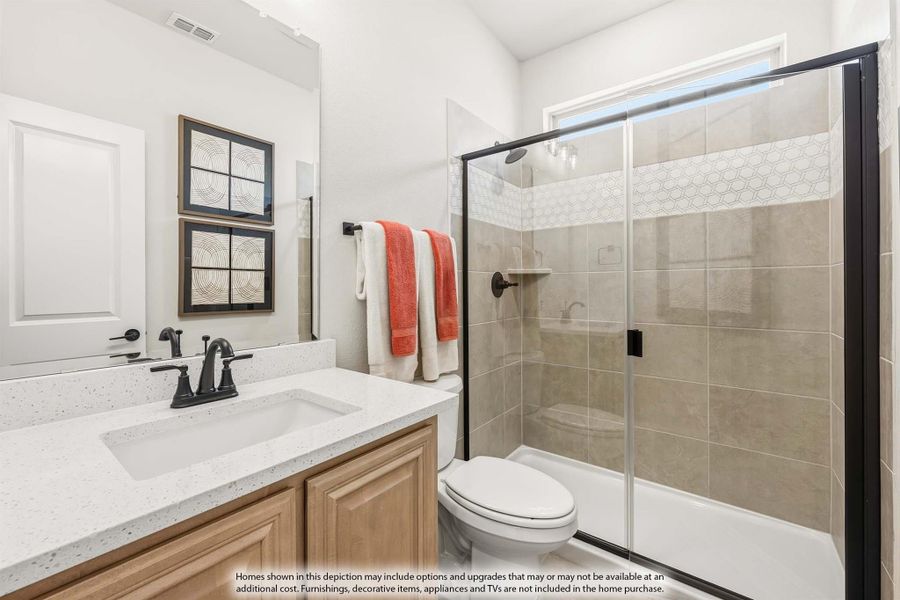Bathroom with quartz vanity, wood cabinets, toilet, and tiled shower with glass door