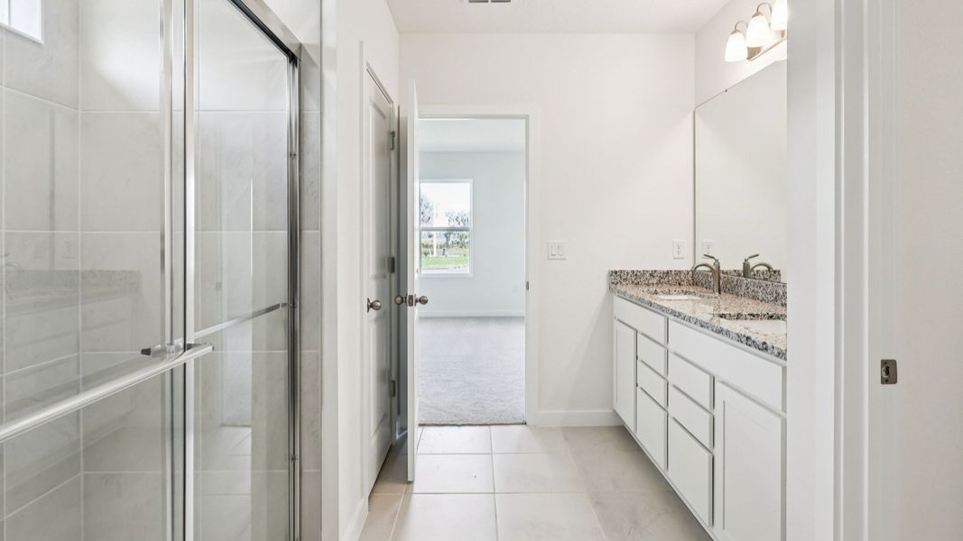 Primary Suite Bathroom with Granite Countertops, Dual Sinks, and White Cabinets in the Baker by DRB Homes Willowbrook North
