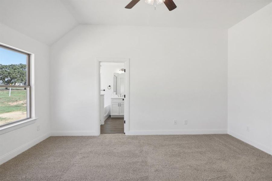 Unfurnished bedroom with ceiling fan, lofted ceiling, ensuite bath, and carpet