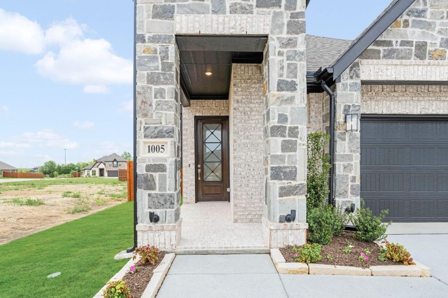 Home entrance with stone columns, wood front door with glass panels, and address number 1005