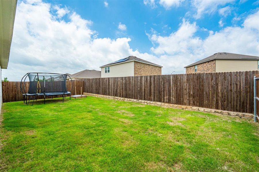 Spacious backyard featuring a wood privacy fence, a stone retaining wall, and a verdant lawn