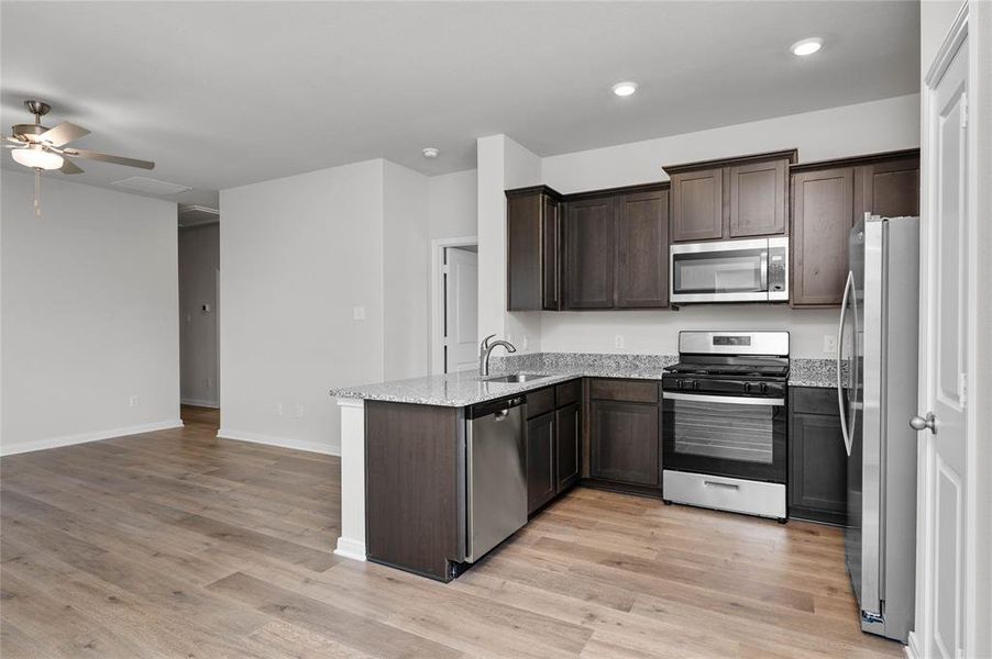 Kitchen with appliances with stainless steel finishes, dark brown cabinets, a peninsula, light wood-style floors, and light stone counters Kitchen with appliances with stainless steel finishes, dark brown cabinets, a peninsula, light wood-style floors, and light stone counters