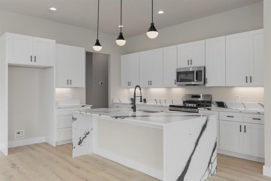 Kitchen with stainless steel appliances, light wood-style flooring, white cabinets, a center island with sink, and light countertops
