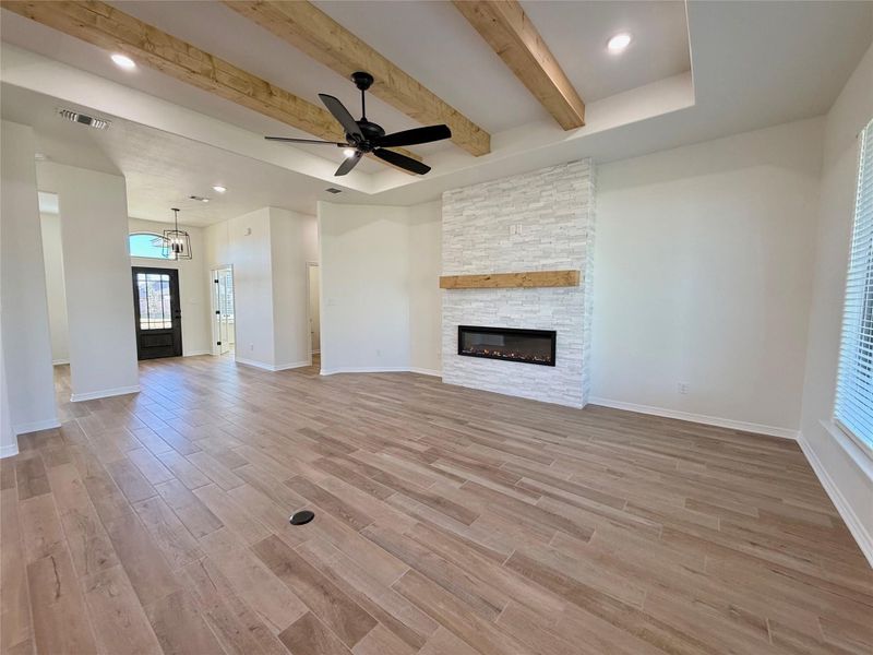 Unfurnished living room with beamed ceiling, light wood finished floors, a stone fireplace, ceiling fan, and a chandelier