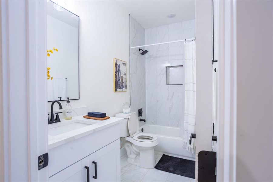 Full bath featuring vanity, shower / bathtub combination with curtain, and light marble finish floors