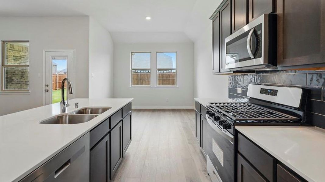 Kitchen featuring a spacious island with dual stainless steel sinks, white countertops, dark cabinetry, stainless steel appliances, and a dark subway tile backsplash