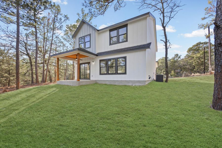 Back of house with a yard, a patio, board and batten siding, and view of wooded area