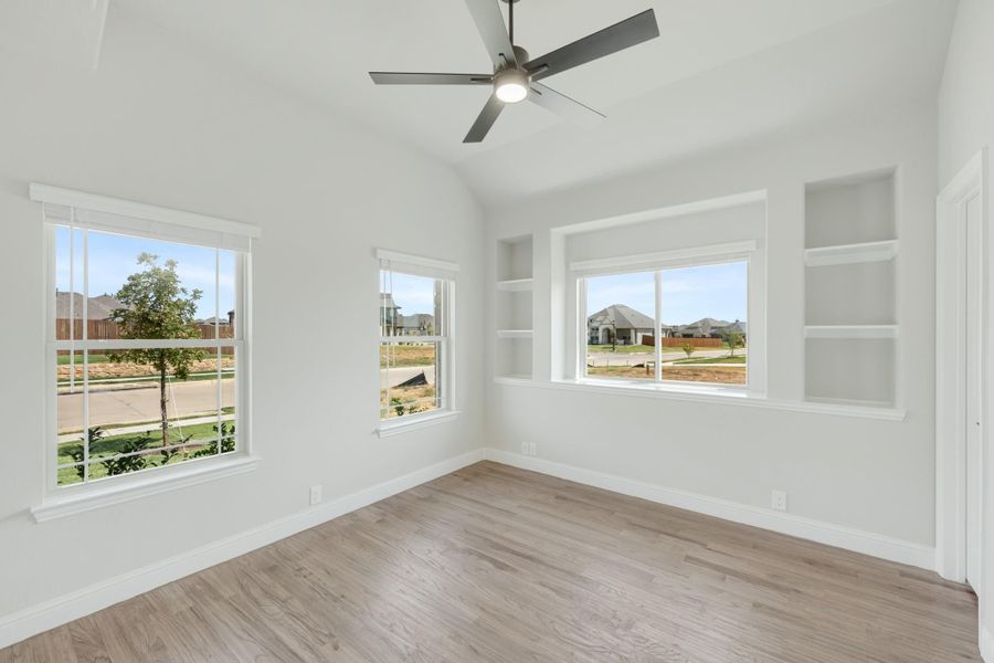 Empty room with vaulted ceiling, ceiling fan, built-in shelves, and hardwood floors with multiple windows Empty room with vaulted ceiling, ceiling fan, built-in shelves, and hardwood floors with multiple windows
