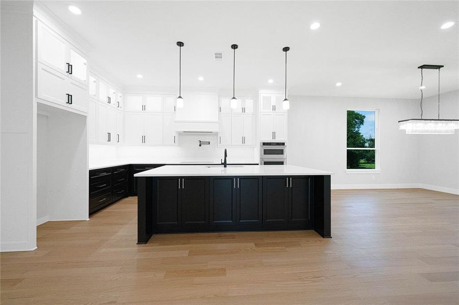 Kitchen with dark cabinetry, baseboards, light wood-type flooring, recessed lighting, and white cabinetry Kitchen with dark cabinetry, baseboards, light wood-type flooring, recessed lighting, and white cabinetry