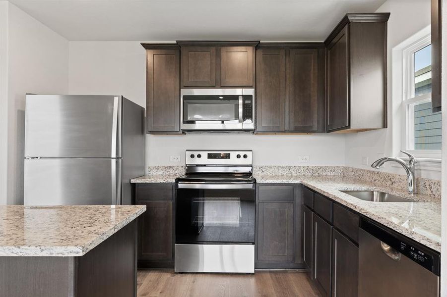 Kitchen featuring light stone countertops, appliances with stainless steel finishes, dark brown cabinetry, sink, and light hardwood / wood-style floors