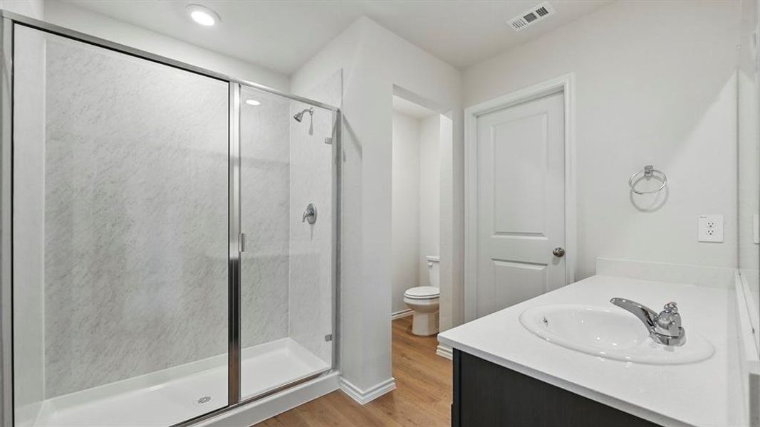 Bathroom featuring a glass-enclosed shower, a vanity with a white countertop and integrated sink, and wood-look flooring