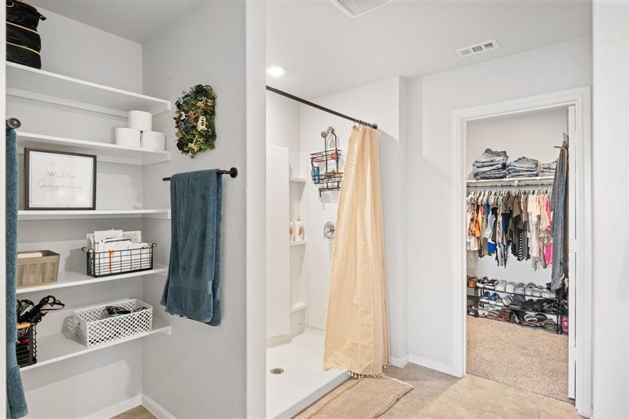 Full bathroom featuring a spacious closet, a stall shower, and light carpet
