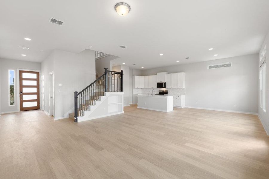 Unfurnished living room featuring plenty of natural light, stairs, light wood-style floors, and recessed lighting