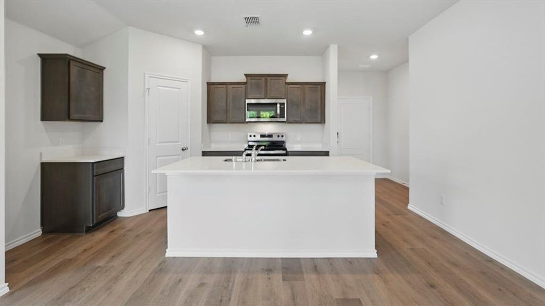 Kitchen with dark wood finish cabinets, stainless steel appliances, an island with sink, light wood-type flooring, and recessed lighting