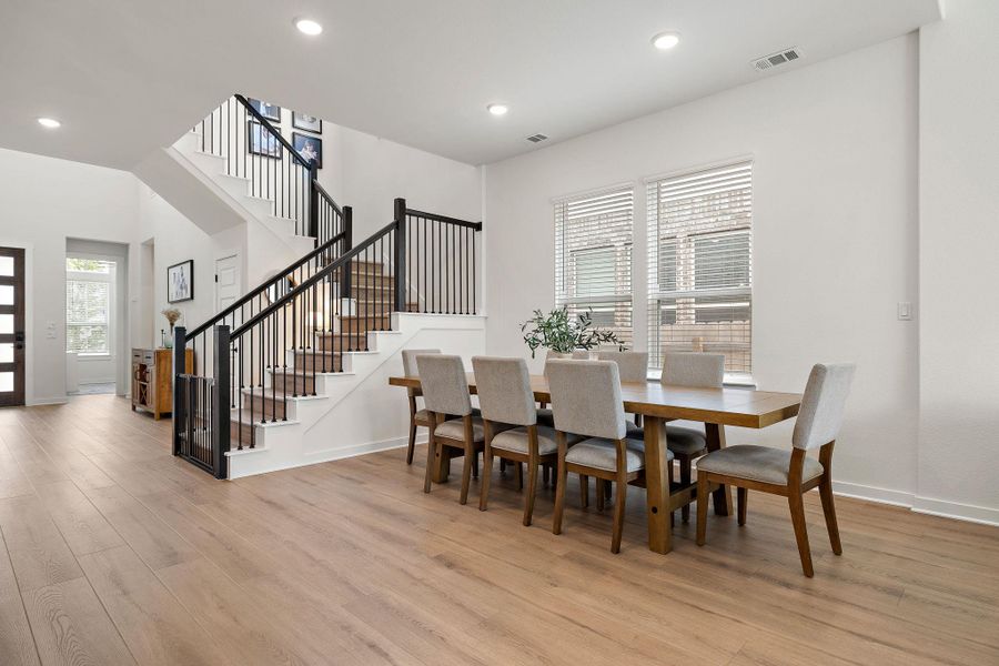 Two-story foyer with natural wood-finish flooring, a contemporary staircase featuring black iron balusters, recessed lighting, and a dining area with dual windows