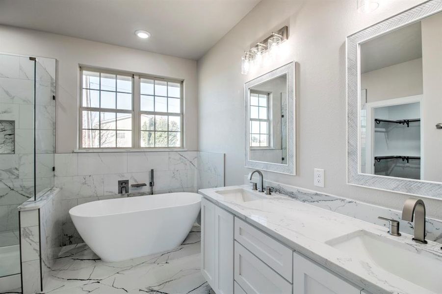 Bathroom with light marble finish floors, plenty of natural light, tile walls, wainscoting, and double vanity