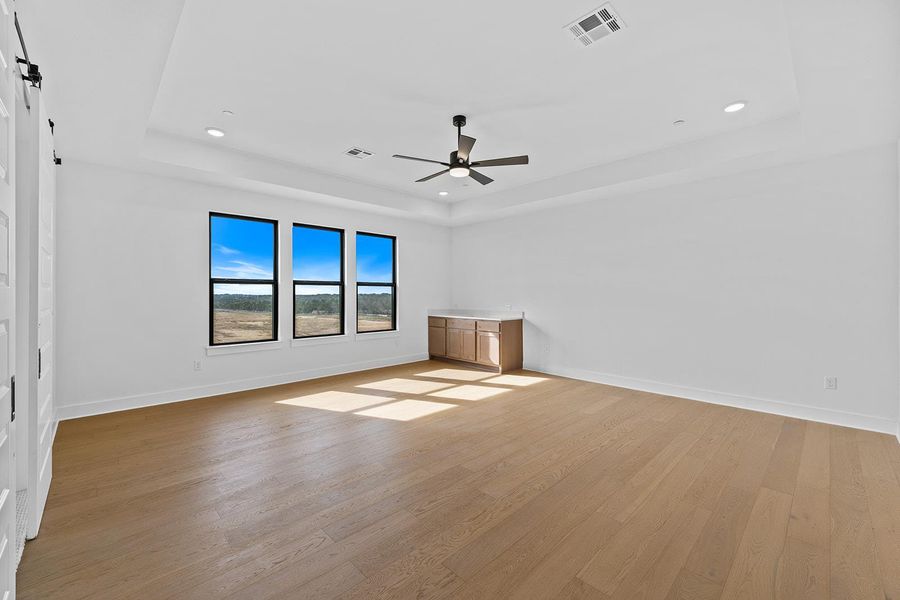 Flex room with light wood finished floors, a tray ceiling, a ceiling fan, recessed lighting, and a barn door
