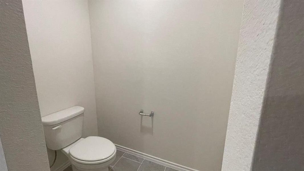 Bathroom featuring a white toilet, light-toned wall paint, and gray floor tiles Bathroom featuring a white toilet, light-toned wall paint, and gray floor tiles