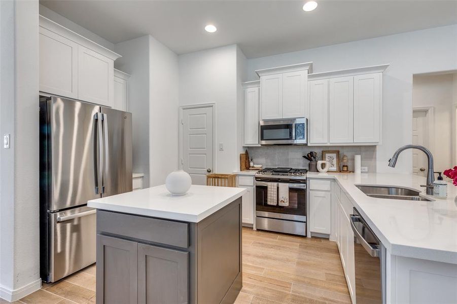 Kitchen featuring appliances with stainless steel finishes, light wood-type flooring, white cabinetry, backsplash, and a kitchen island