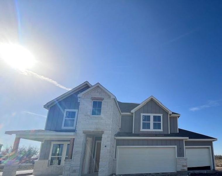 View of front of house with an attached garage, stone siding, and board and batten siding