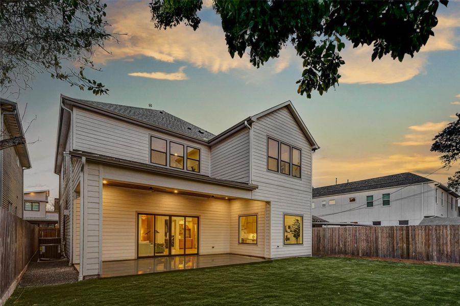 Beautiful rear elevation showcasing the home’s clean modern lines and expansive covered patio. Large sliding glass doors create seamless indoor-outdoor flow, while upstairs windows flood both levels with natural light.
