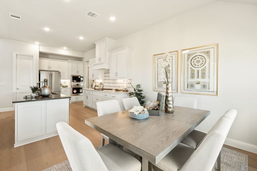 Open dining area with wood table and white chairs adjacent to kitchen with white cabinets and hardwood floors