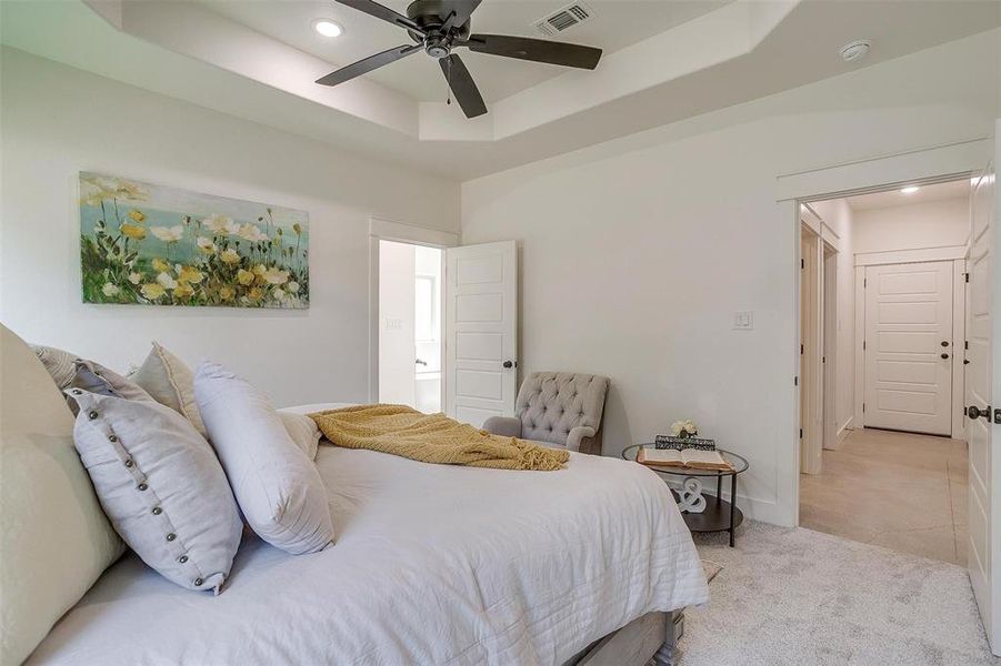 Bedroom with ceiling fan, light carpet, and a tray ceiling