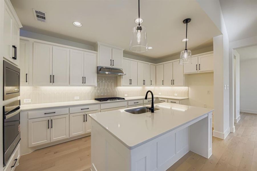 Kitchen with an island with sink, light wood-style floors, and white cabinets