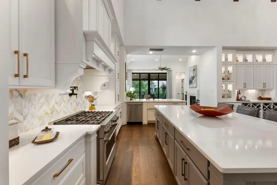 The cooking area is thoughtfully designed with upgraded cabinetry, a marble backsplash, pot filler, and a clear view through the main living spaces. Pull-out shelving, cabinet lighting, and expanded storage add function behind the polished finish.