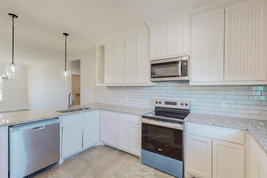 Kitchen with backsplash, sink, decorative light fixtures, white cabinetry, and stainless steel appliances