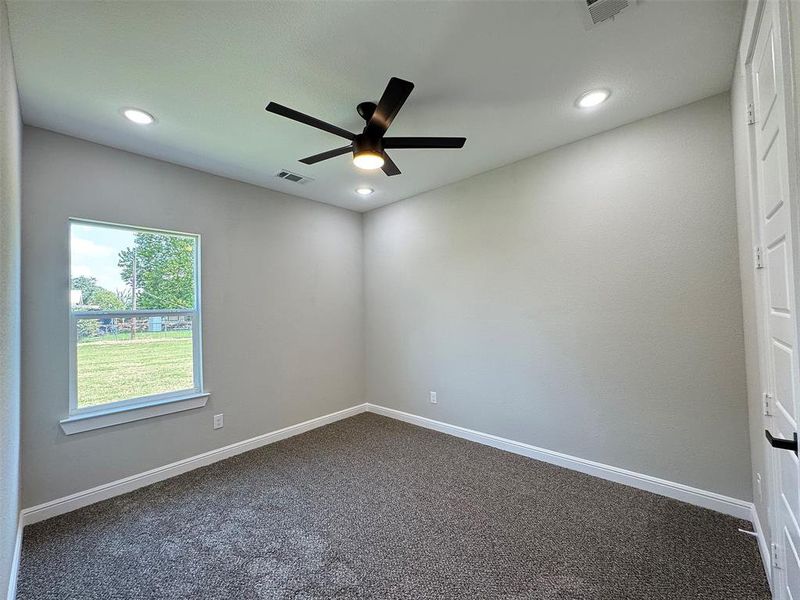 Carpeted room featuring a ceiling fan with integrated lighting, recessed ceiling lights, a window with exterior landscape, and a paneled door with a black handle