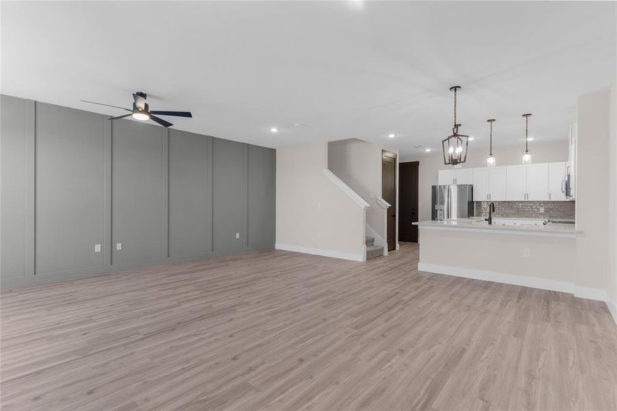 Spacious living area featuring wood-finish flooring, a contemporary accent wall with vertical paneling, and a modern ceiling fan