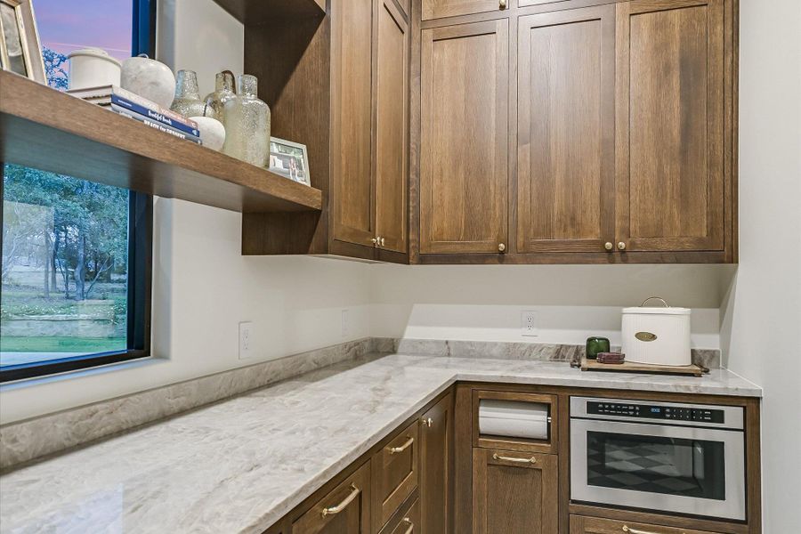 Kitchen with open shelves, light stone counters, and brown cabinetry Kitchen with open shelves, light stone counters, and brown cabinetry