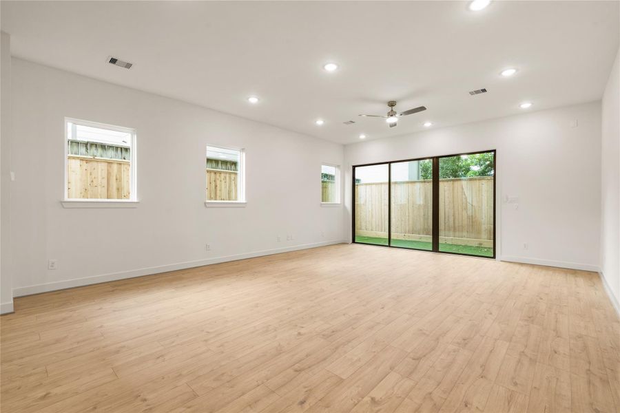 Expansive open living space — continuous oak-look flooring, multiple side windows providing balanced natural light, and modern ceiling fan detail.