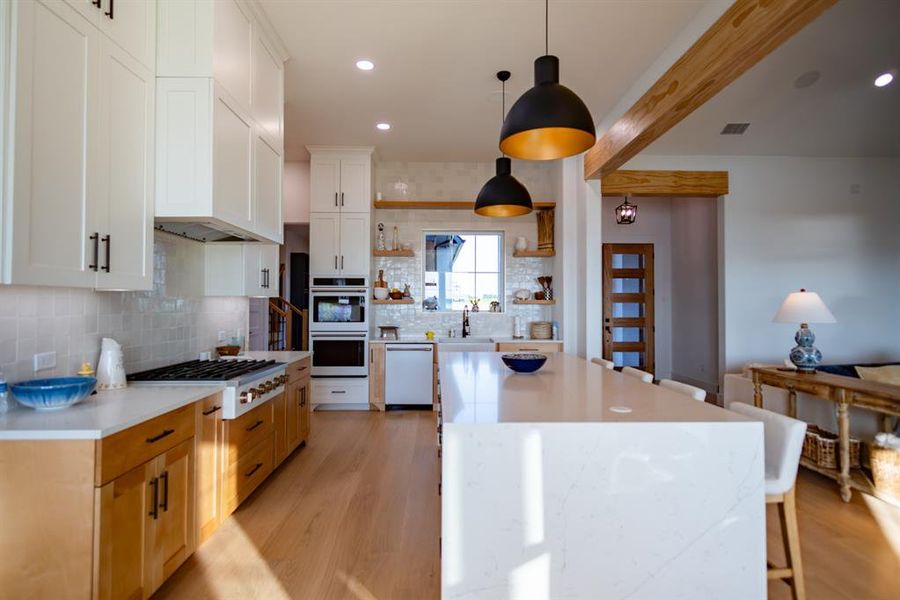 Kitchen with open shelves, light wood-style flooring, backsplash, a breakfast bar, and decorative light fixtures Kitchen with open shelves, light wood-style flooring, backsplash, a breakfast bar, and decorative light fixtures