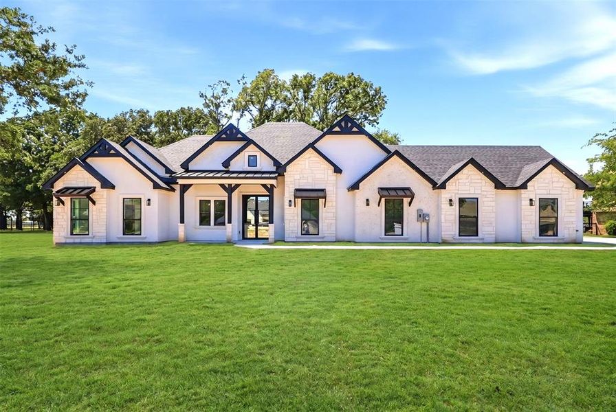 Contemporary ranch-style residence featuring a white stucco and stone exterior, dark trim accents, a prominent covered entry, black-framed windows, and decorative window awnings