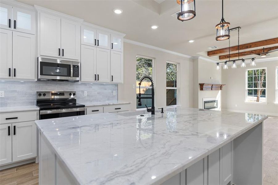 Kitchen with white cabinetry, ornamental molding, hanging light fixtures, and appliances with stainless steel finishes