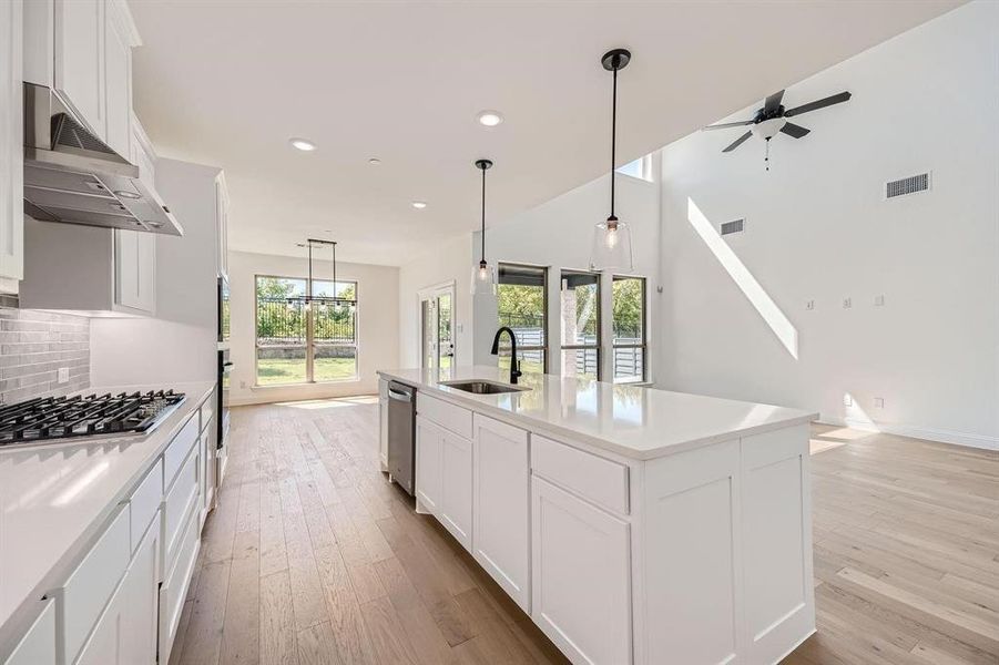 Modern kitchen featuring white shaker cabinetry, stainless steel appliances, a center island with sink, and light wood-finish flooring Modern kitchen featuring white shaker cabinetry, stainless steel appliances, a center island with sink, and light wood-finish flooring