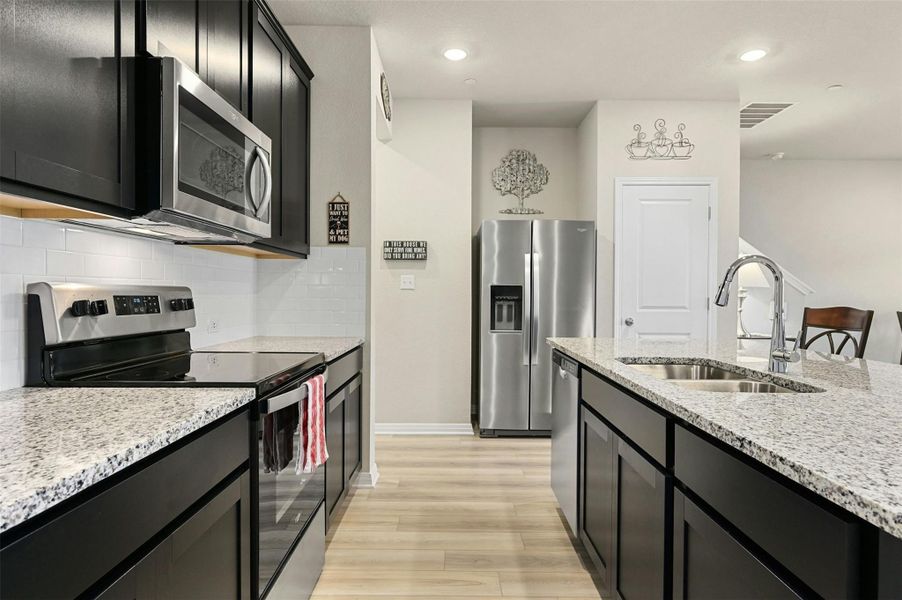 Kitchen featuring light stone countertops, appliances with stainless steel finishes, decorative backsplash, sink, and light hardwood / wood-style flooring