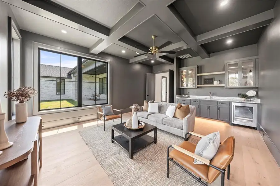 Living area with light wood-style floors, wine cooler, coffered ceiling, beamed ceiling, and bar with sink