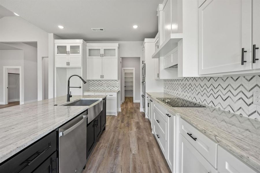 Kitchen featuring dark cabinetry, light stone countertops, dishwasher, glass insert cabinets, and recessed lighting
