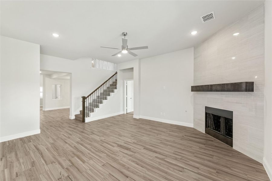 Open living room with hardwood floors, white brick fireplace, ceiling fan, and staircase leading to second floor.