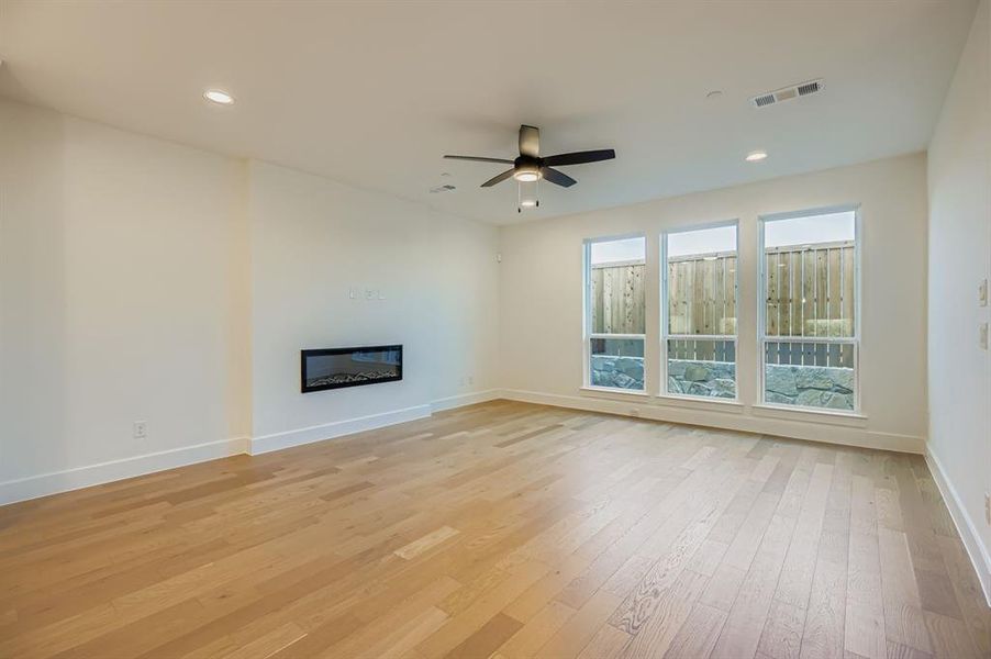 Unfurnished living room featuring a glass covered fireplace, light wood-style flooring, recessed lighting, and a ceiling fan Unfurnished living room featuring a glass covered fireplace, light wood-style flooring, recessed lighting, and a ceiling fan