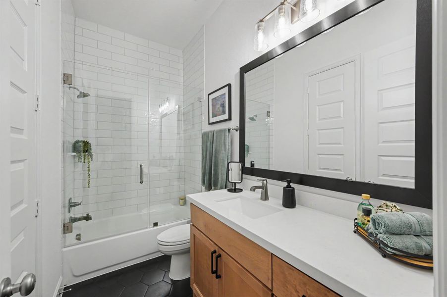 This bathroom has been appointed with the same upgrades as the other two full baths. The vanity has a maple stain, large quartz counter top with under mount sink and black hardware. There are octagonal shaped tiles on the floor and the shower subway tile goes to the ceiling. The glass tub enclosure was added and the mirror is framed, and the light fixture an upgrade. The closet is located in the bathroom. This bathroom has been appointed with the same upgrades as the other two full baths. The vanity has a maple stain, large quartz counter top with under mount sink and black hardware. There are octagonal shaped tiles on the floor and the shower subway tile goes to the ceiling. The glass tub enclosure was added and the mirror is framed, and the light fixture an upgrade. The closet is located in the bathroom.