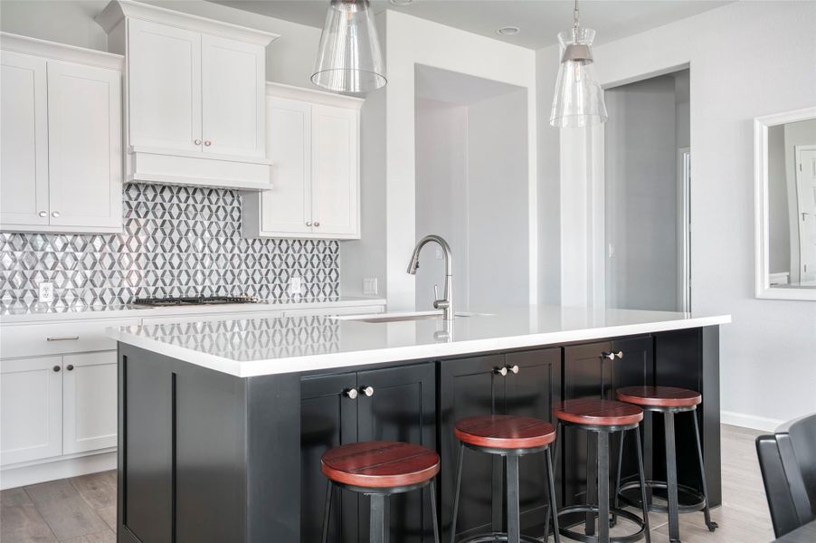 Modern kitchen with a sleek design featuring white cabinetry, a striking geometric backsplash, and a large island with a quartz countertop. The island includes a built-in sink and seating with stylish barstools, complemented by pendant lighting. Modern kitchen with a sleek design featuring white cabinetry, a striking geometric backsplash, and a large island with a quartz countertop. The island includes a built-in sink and seating with stylish barstools, complemented by pendant lighting.