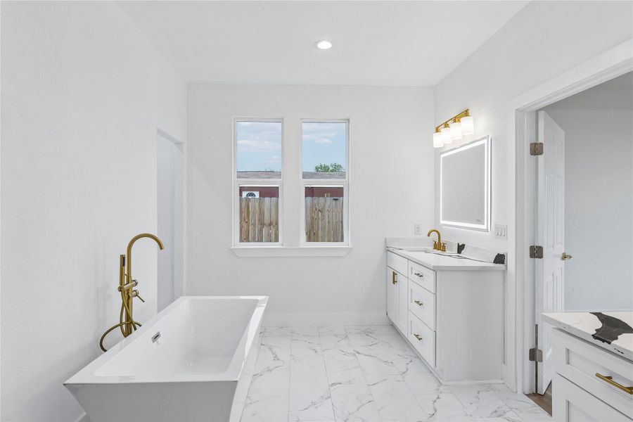 A well-lit primary bathroom featuring a freestanding soaking tub and a pristine vanity.